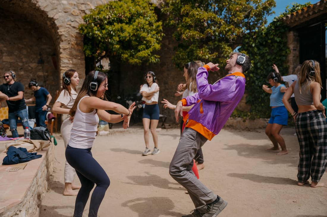Personas bailando con auriculares AURA en un patio soleado
